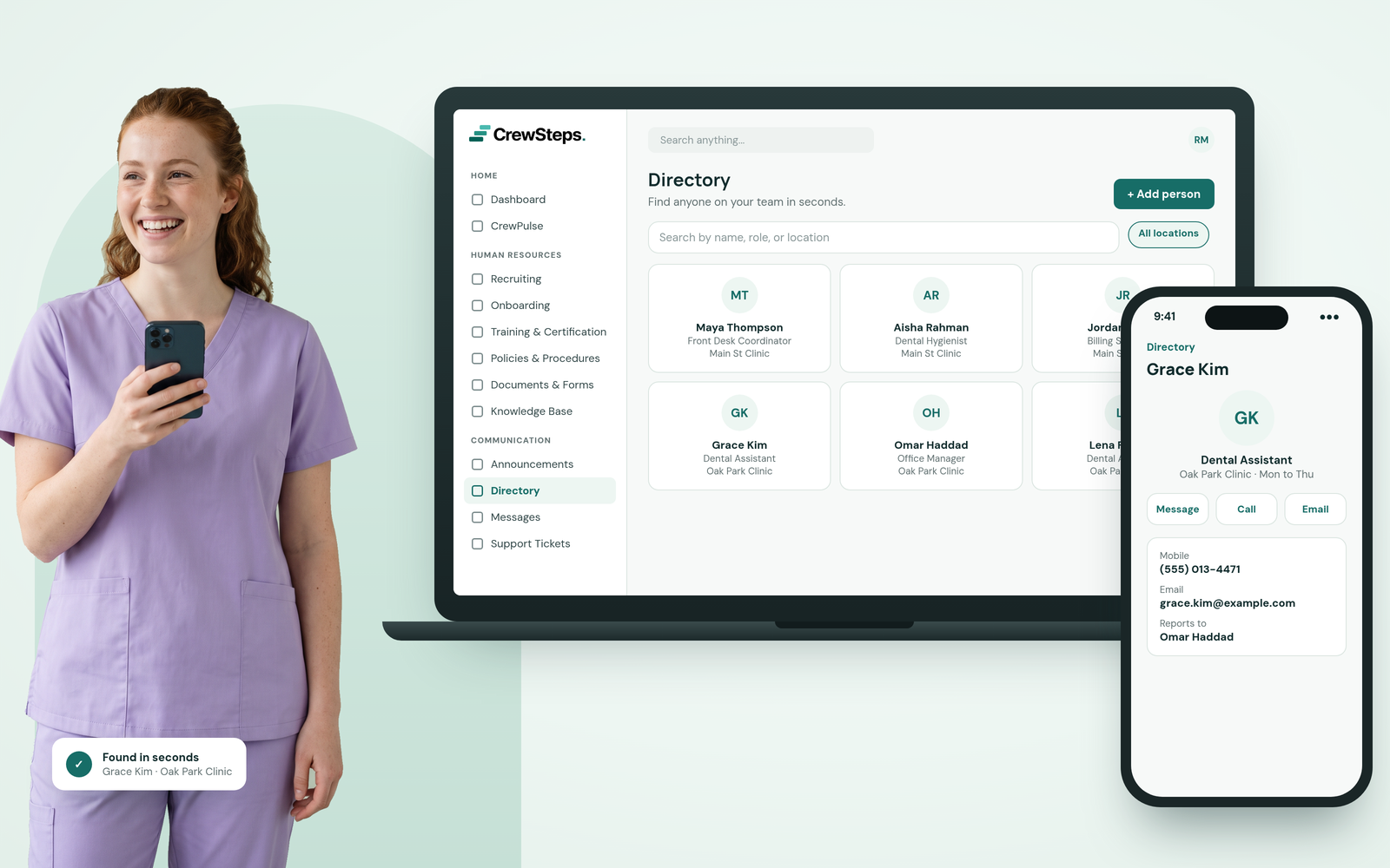 A smiling dental assistant with auburn hair in lavender scrubs holding her phone beside a CrewSteps laptop showing a team directory and a phone with a coworker's contact card.