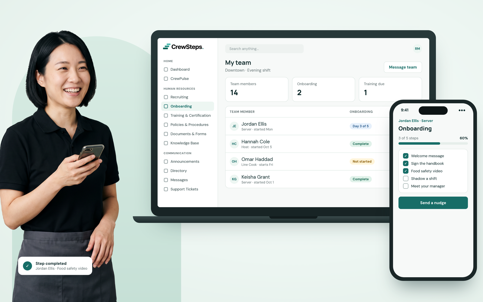 A laughing restaurant shift manager in a black polo holding her phone beside a CrewSteps laptop showing her team’s onboarding status and a phone with a new server’s onboarding steps.
